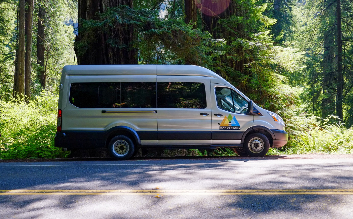 A silver Wandervans RV rental parked on a forest road amidst tall redwood trees, ready for an outdoor adventure.