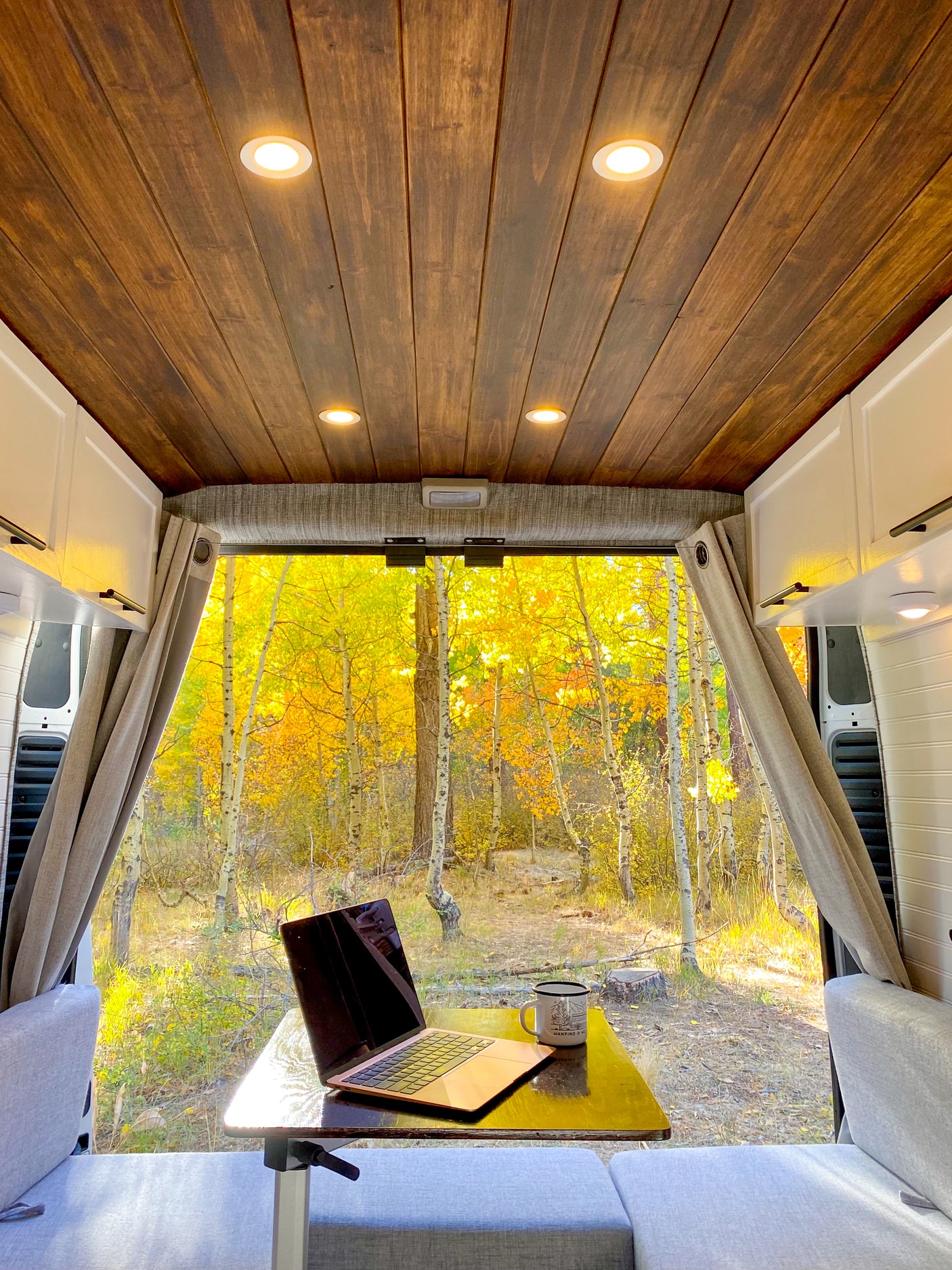 Cozy RV rental interior with laptop & mug, facing a vibrant golden aspen forest. Ideal for a nature-filled mobile office.