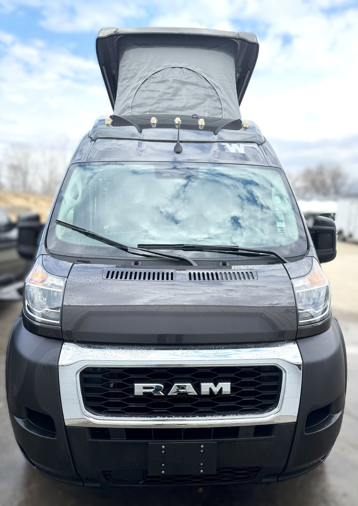 Front view: Rainy dark grey Ram ProMaster camper van with pop-top roof, ready for your next RV rental adventure.