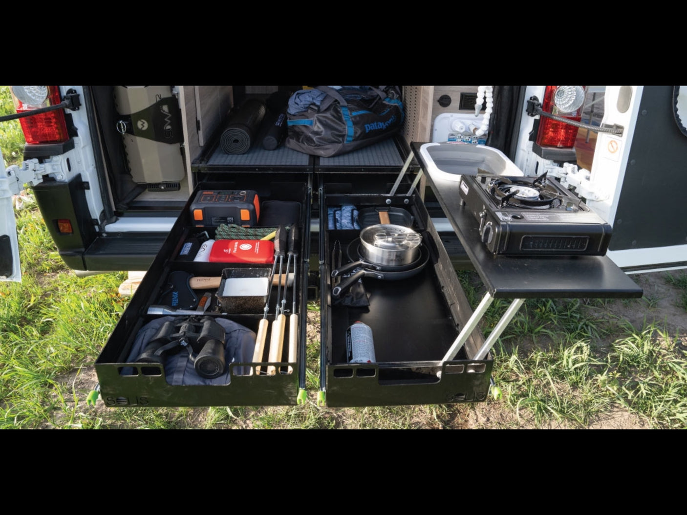 RV rental: Camper van's integrated rear kitchen features pull-out drawers with stove, sink, and organized camping gear.