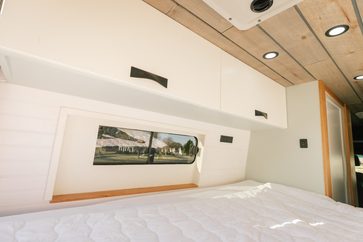 Bright RV rental bedroom features a cozy bed, overhead cabinets, and a window for scenic views.