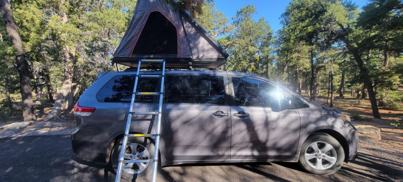 parked in a sunny forest campsite. A unique RV rental for nature adventures.|Minivan with a rooftop tent set up in a sunny forest. Ladder extends to ground for this RV rental.|Explore the outdoors! Grey minivan with rooftop tent set up in a sunny pine forest. A flexible alternative to an RV rental.|Grey minivan with rooftop tent pitched at a sunny campground surrounded by trees. A great RV rental alternative for outdoor adventures.|Open vehicle rooftop tent with a mattress and mesh window — photo 4