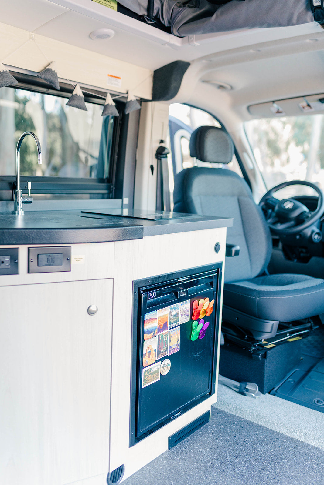 Inside an RV rental: a compact kitchen with sink, induction cooktop, and fridge adorned with travel magnets.