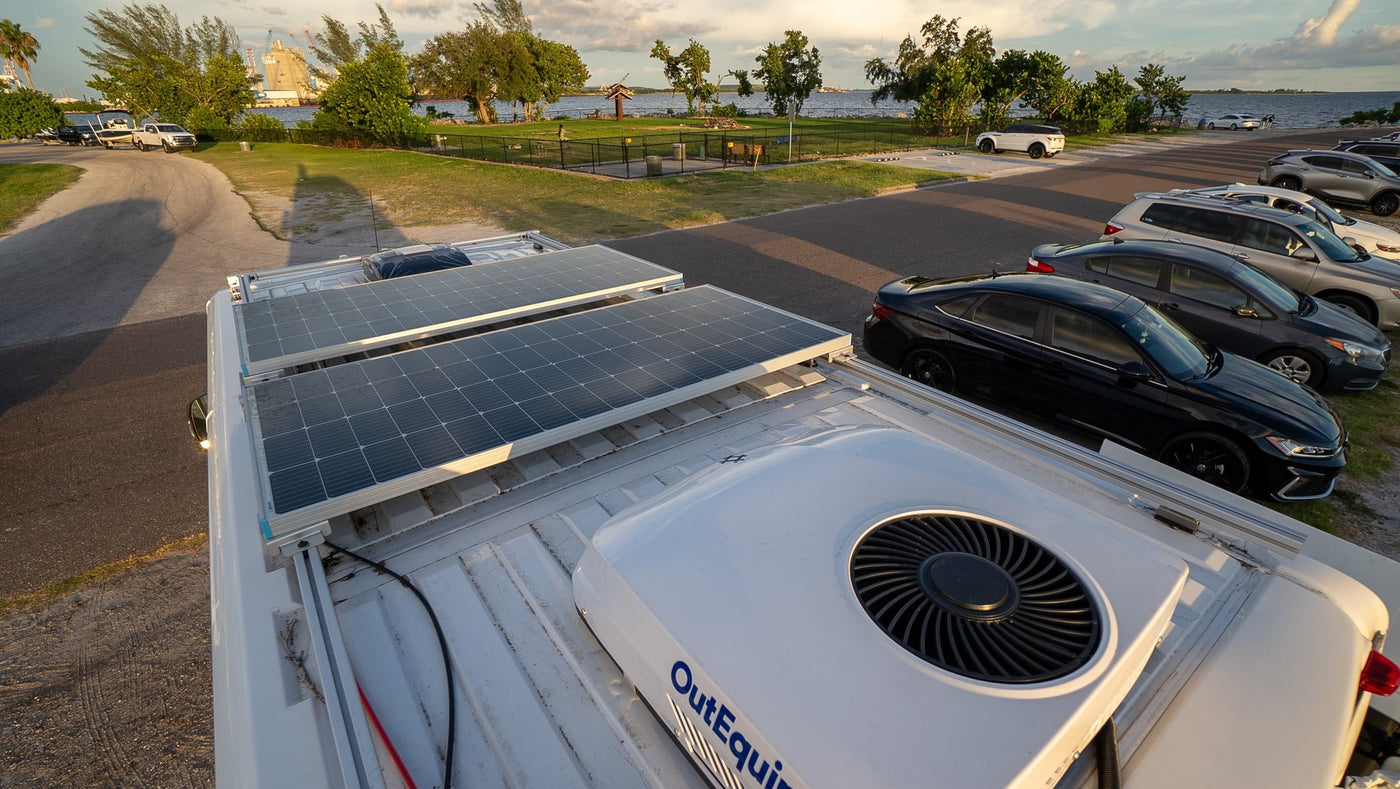 Top-down view of an RV rental roof with two solar panels and an OutEquip AC unit, parked by a waterfront scenic park. — photo 8
