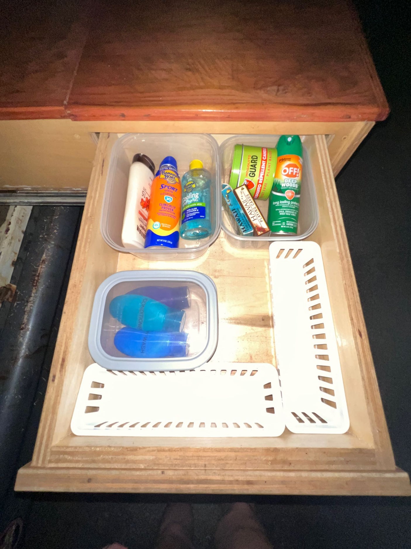 This rv rental drawer holds organized travel toiletries, sunscreen, bug spray, and Hawaii playing cards, perfect for outdoor adventures.