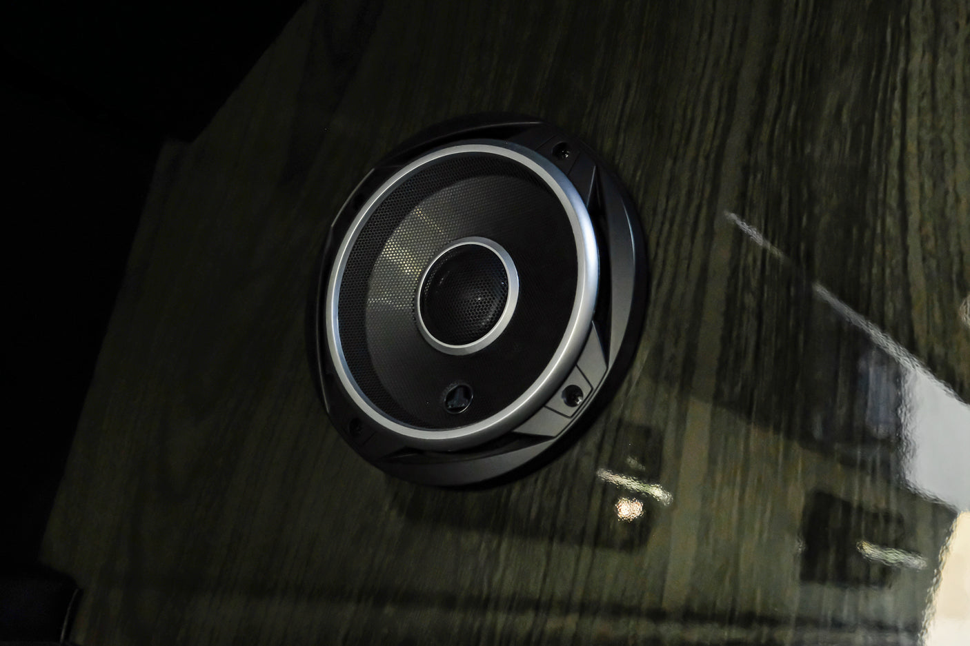 Close-up of a circular speaker with silver trim, installed in a dark wood panel, typical of an RV rental interior.