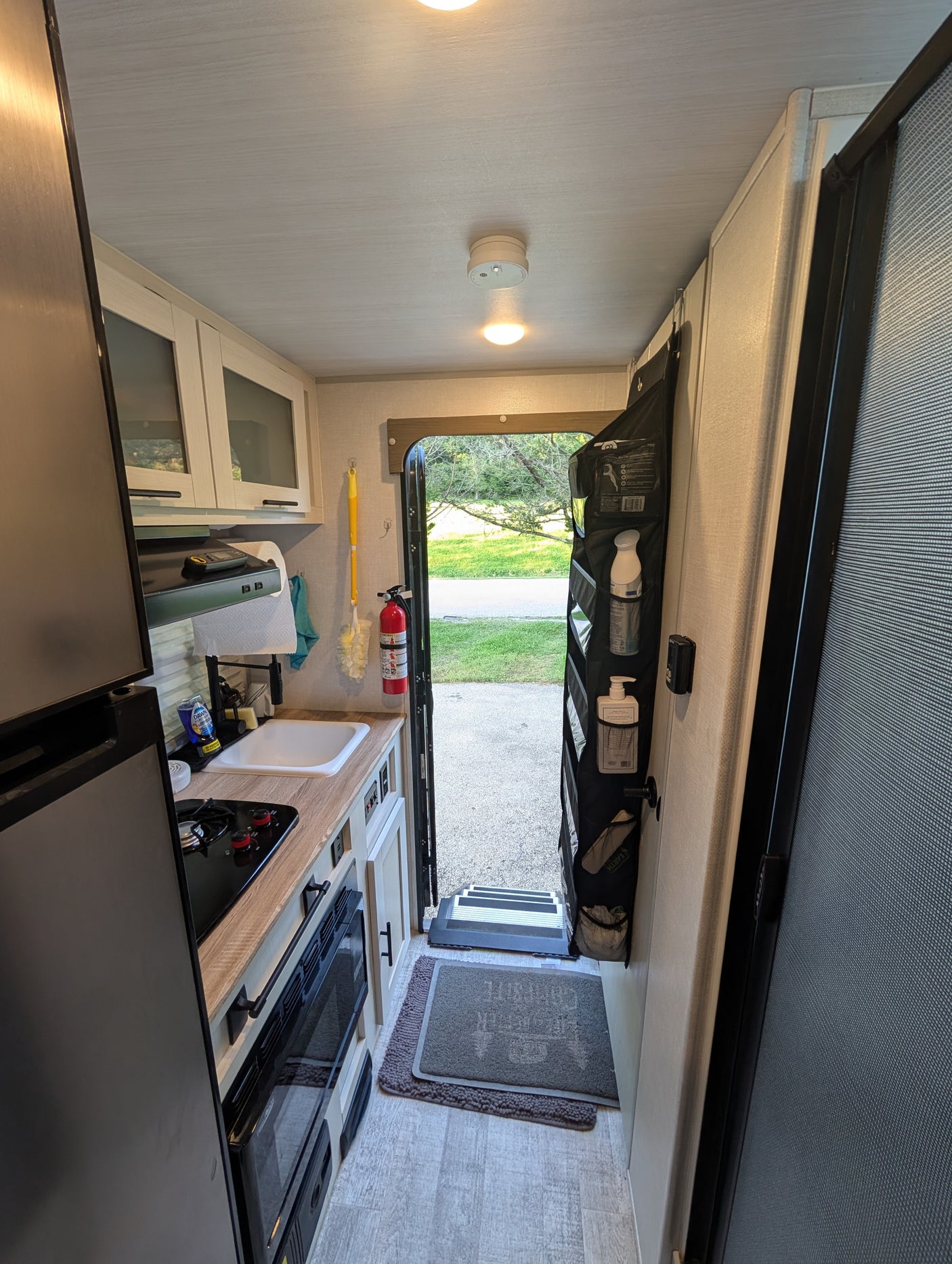 This rv rental shows a compact kitchen with a fridge, sink, and stove, leading to an open entryway with hanging storage.