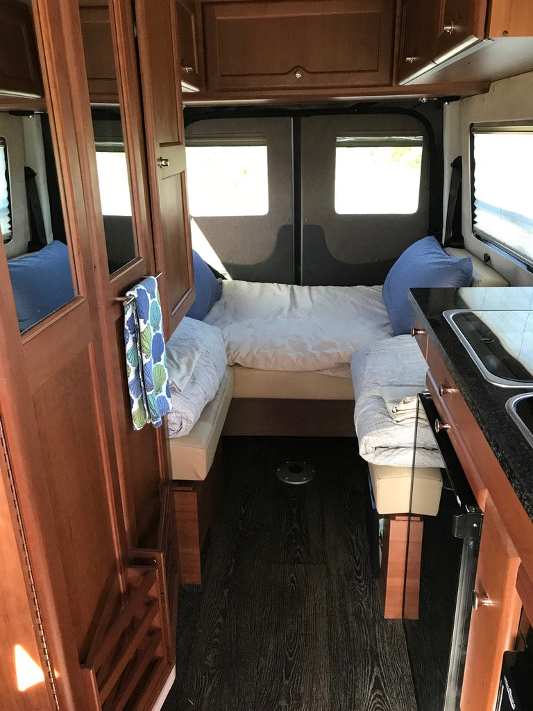 Step inside this RV rental: a cozy interior featuring a bed area, kitchen counter, and wood cabinetry. Perfect for travel.