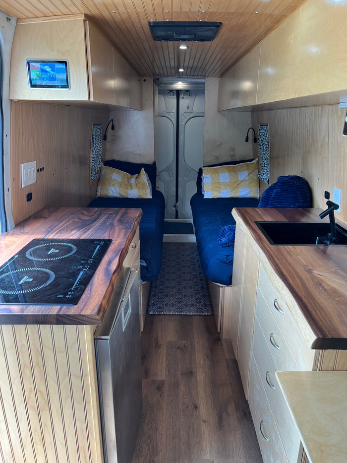 This RV rental interior features a compact kitchen with cooktop/sink, cozy twin beds, and smart controls, perfect for travel.