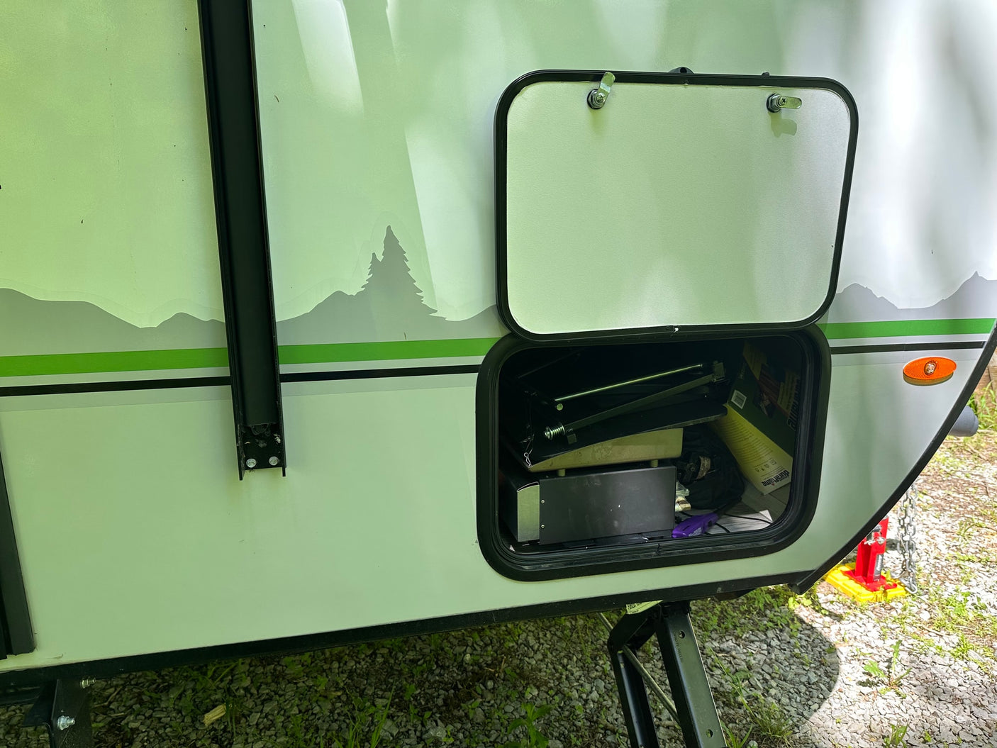 RV rental with open storage hatch displaying outdoor gear & nature-themed decals on its side.