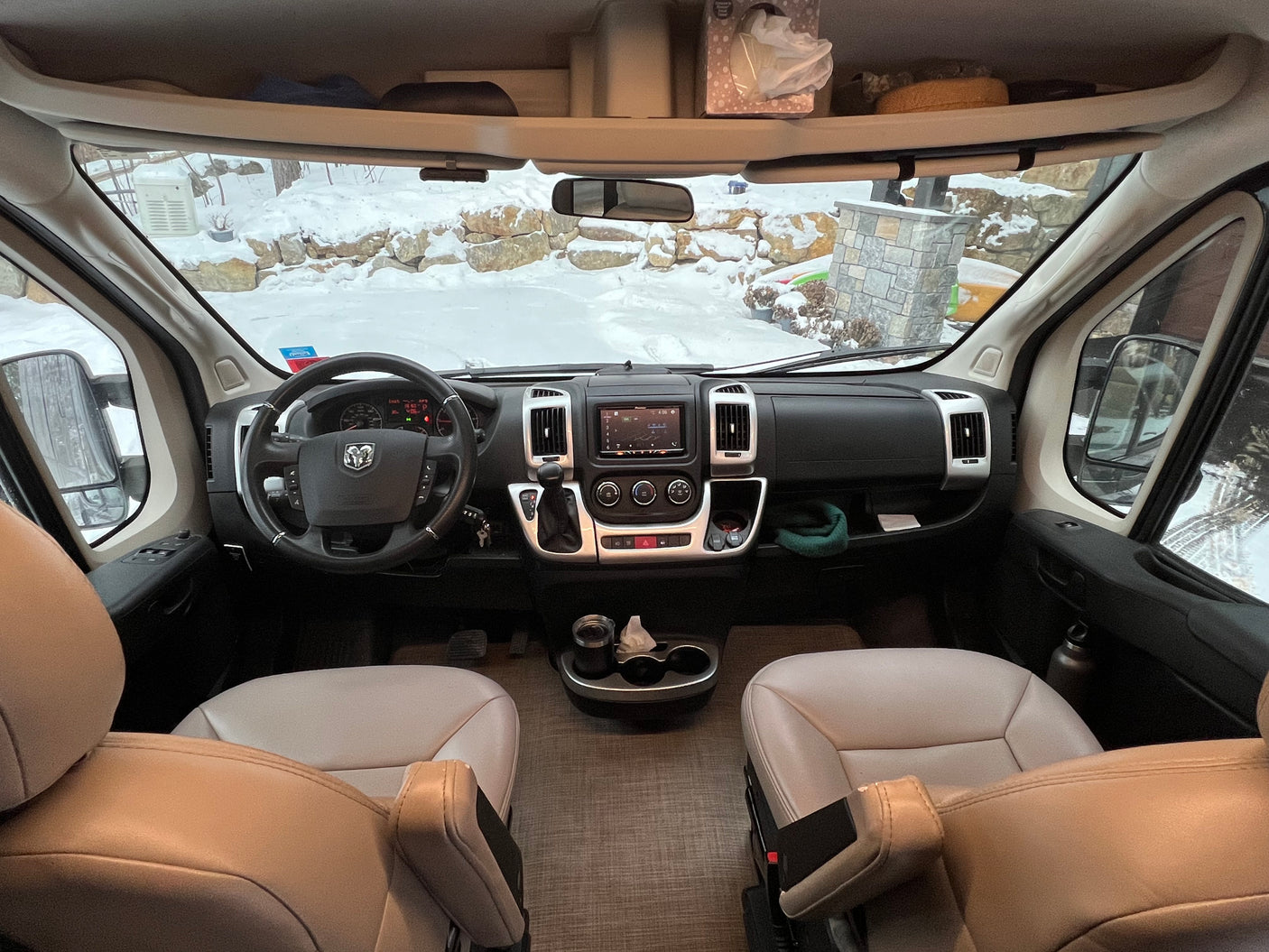Cozy rv rental interior looking out at a snowy winter landscape. Dashboard, steering wheel, and front seats visible.