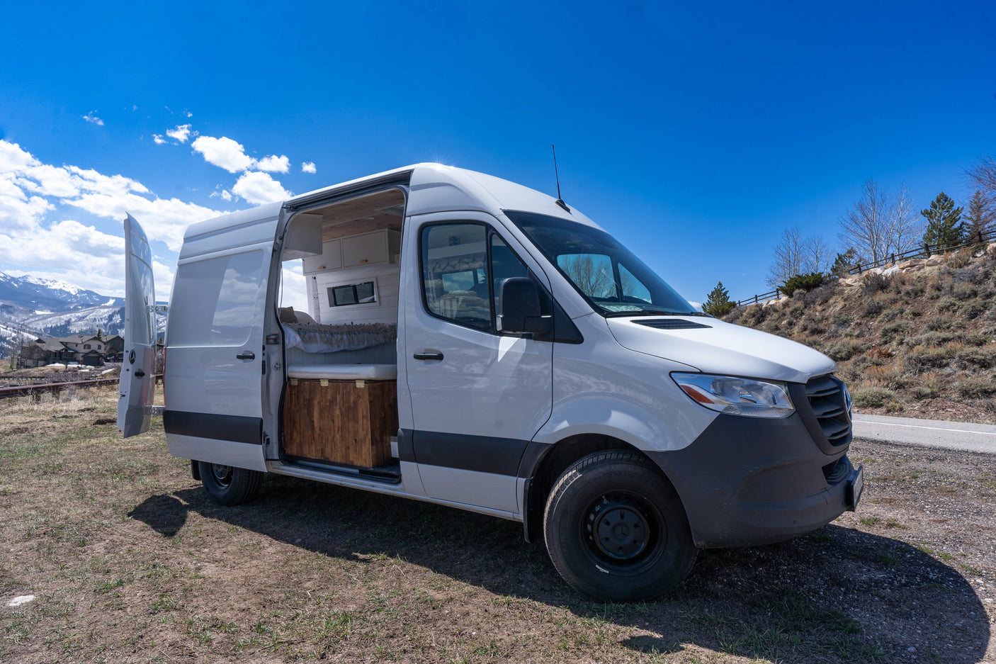 This white RV rental camper van is parked outdoors with its doors open, revealing its custom interior conversion.