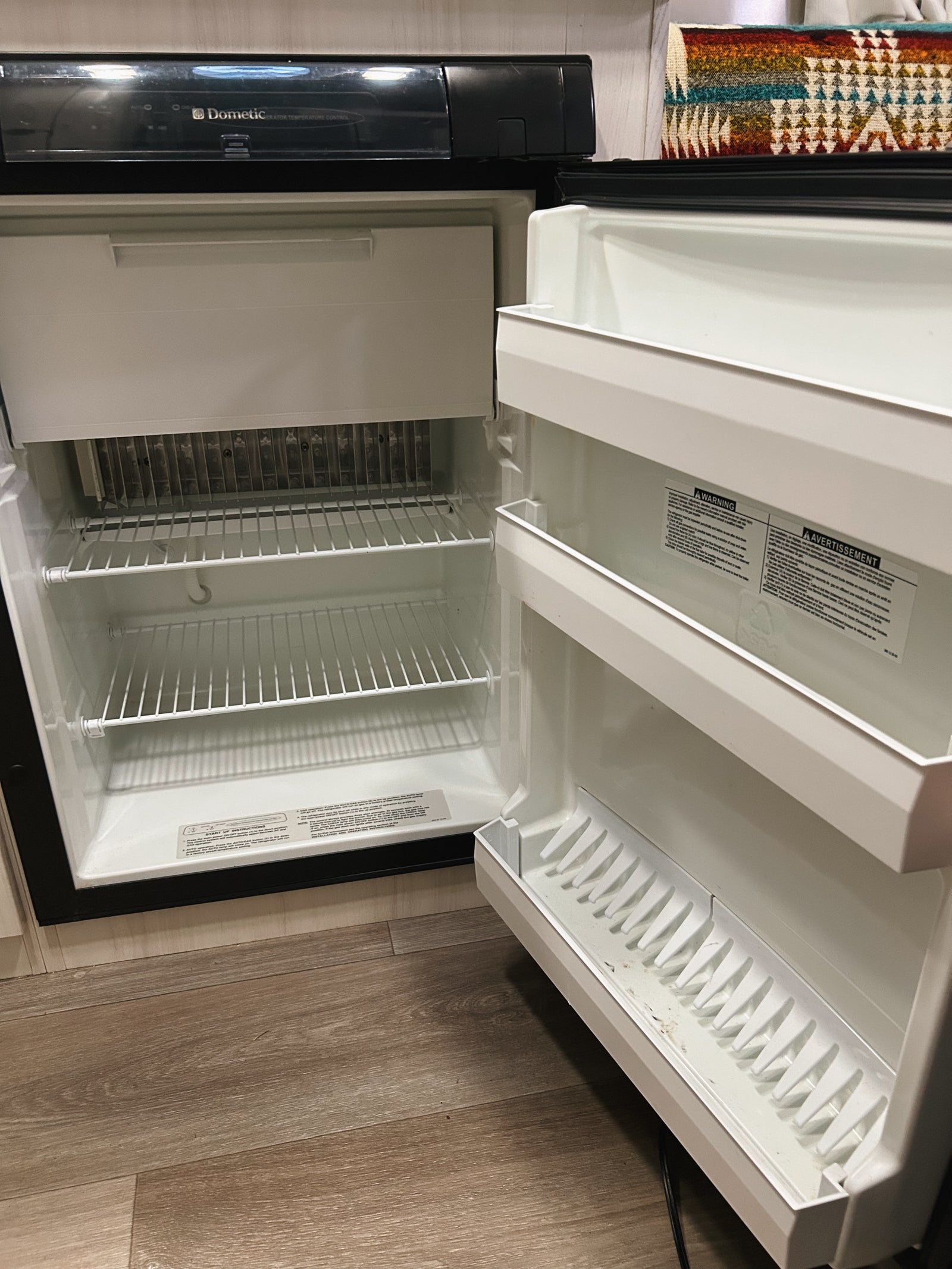 Empty Dometic refrigerator with an open door, revealing its clean, white interior and wire shelves, typical in an rv rental.