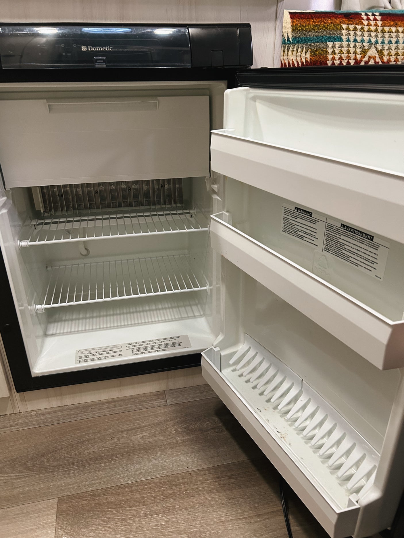 Empty Dometic refrigerator with an open door, revealing its clean, white interior and wire shelves, typical in an rv rental.