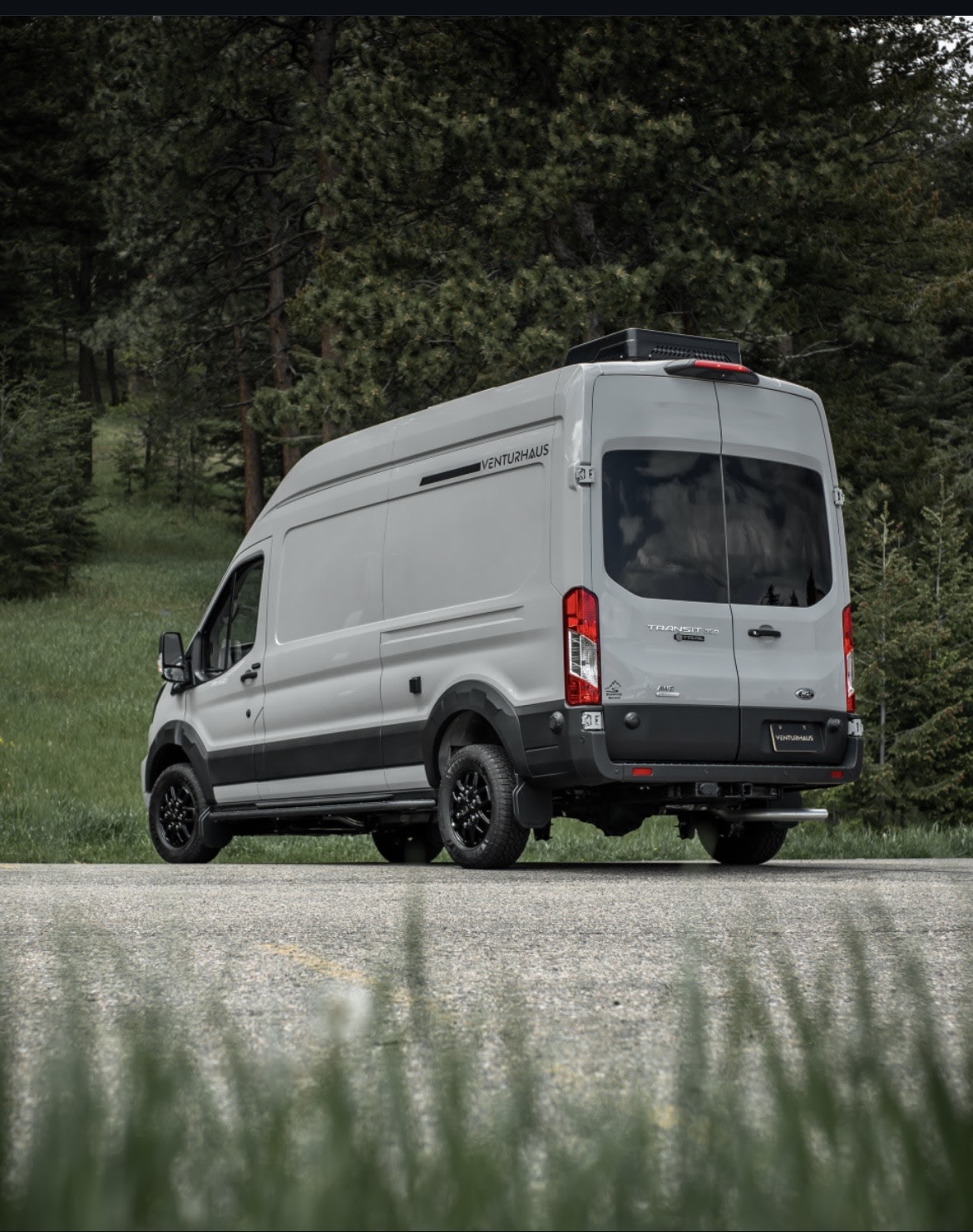 Light gray Venturhaus Ford Transit campervan, customized for adventure rv rental, parked by a forest.