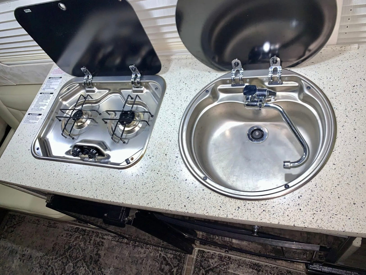 Compact rv rental kitchenette with a two-burner stove, sink, and open lids. Perfect for camper van cooking.
