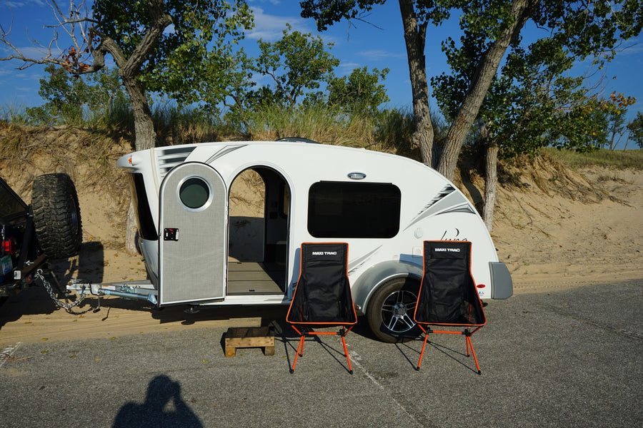Teardrop RV rental parked by sandy dunes. Open door