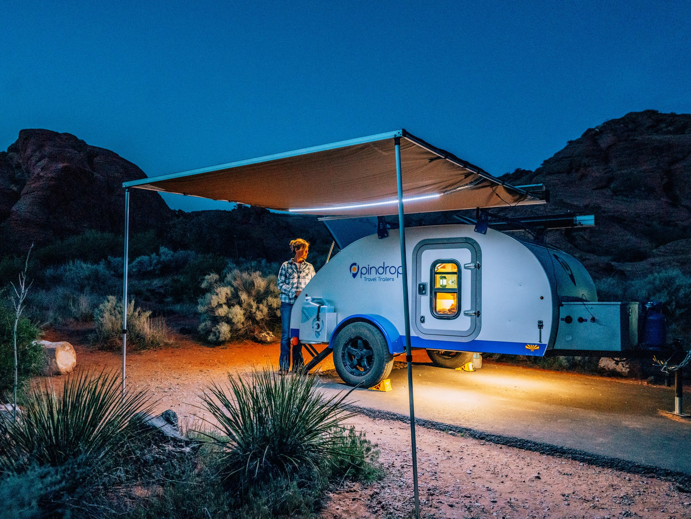 Night camping with a Pindrop teardrop **rv rental** under an illuminated awning, a person stands beside it in the desert. — photo 12