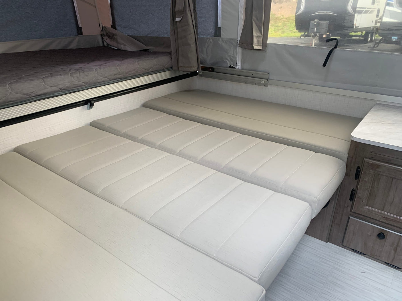 RV rental interior: bed with gray mattress & versatile light-colored cushions for seating or sleeping.