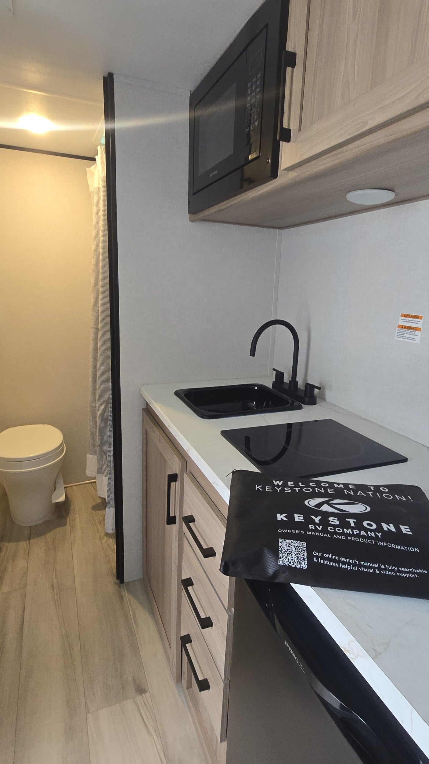 RV rental interior features a modern, compact kitchen with a sink, cooktop, microwave, fridge, and adjacent bathroom.