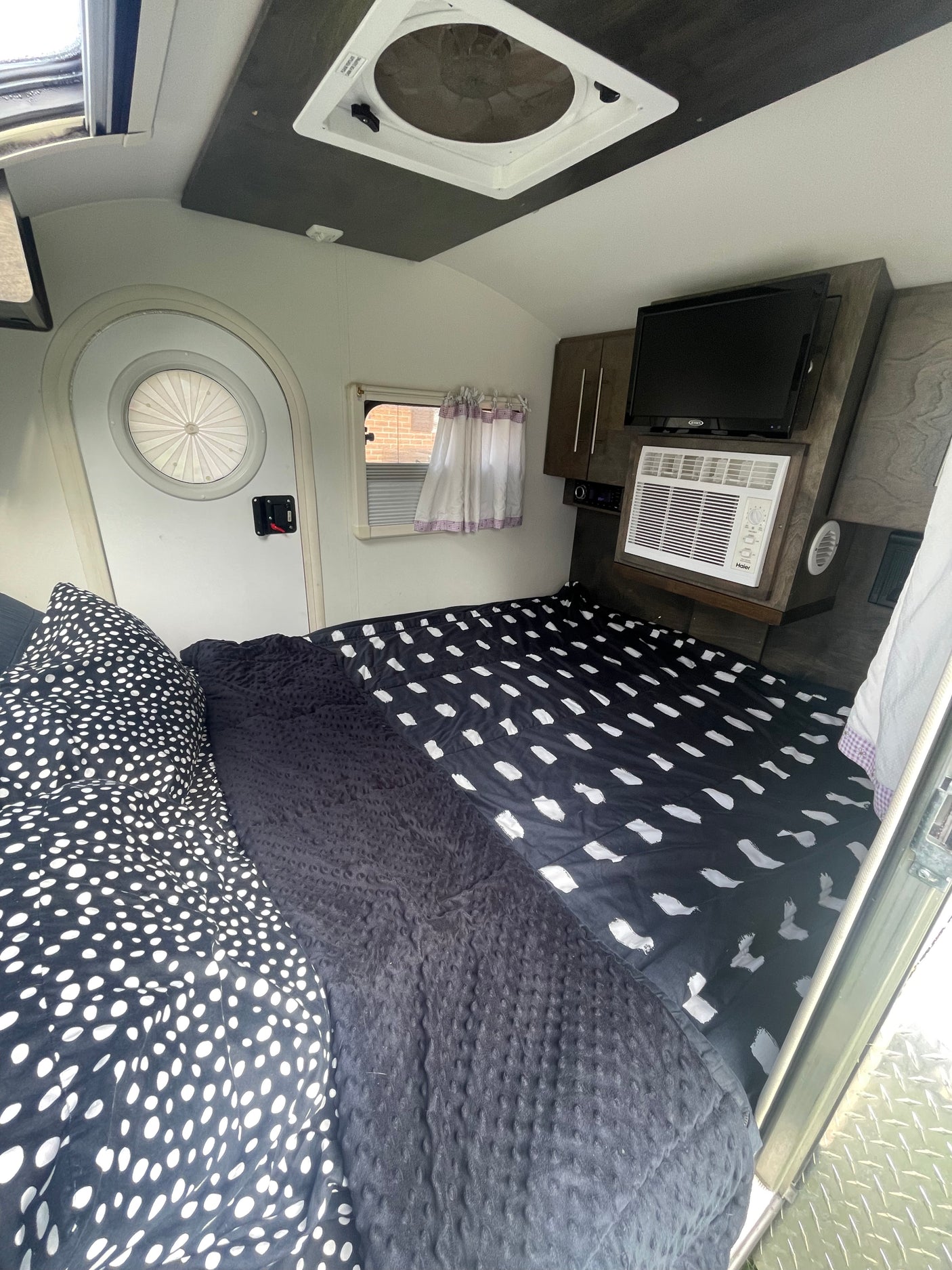 Cozy RV rental interior featuring a patterned bed, mounted TV, AC unit, and a distinctive round door.