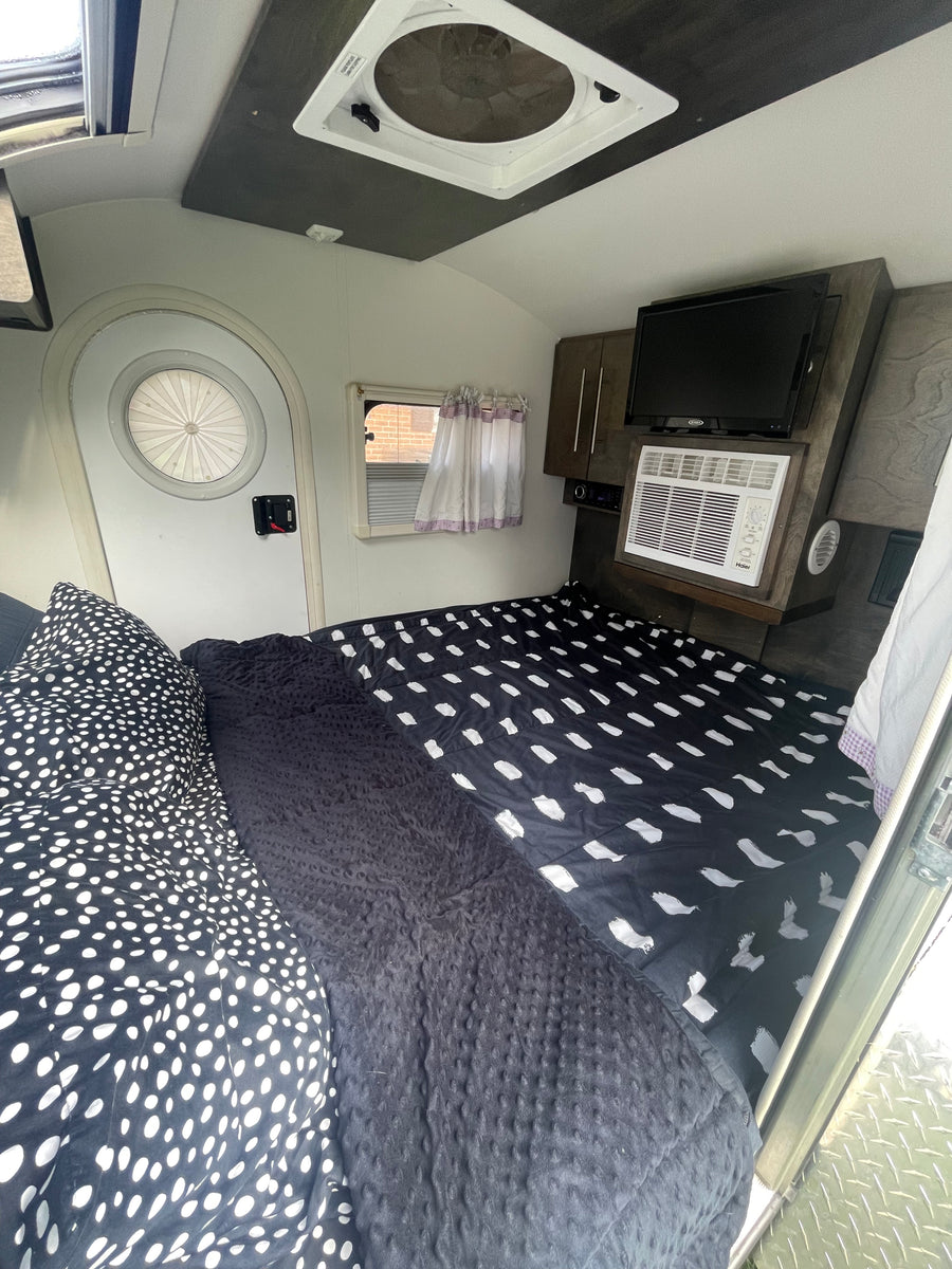 Cozy RV rental interior featuring a patterned bed, mounted TV, AC unit, and a distinctive round door.