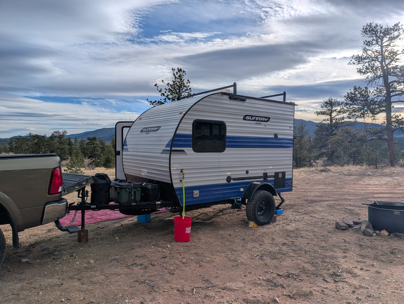 RV rental camping setup: Sunray Sport travel trailer with a truck in a rustic mountain setting under a cloudy sky.