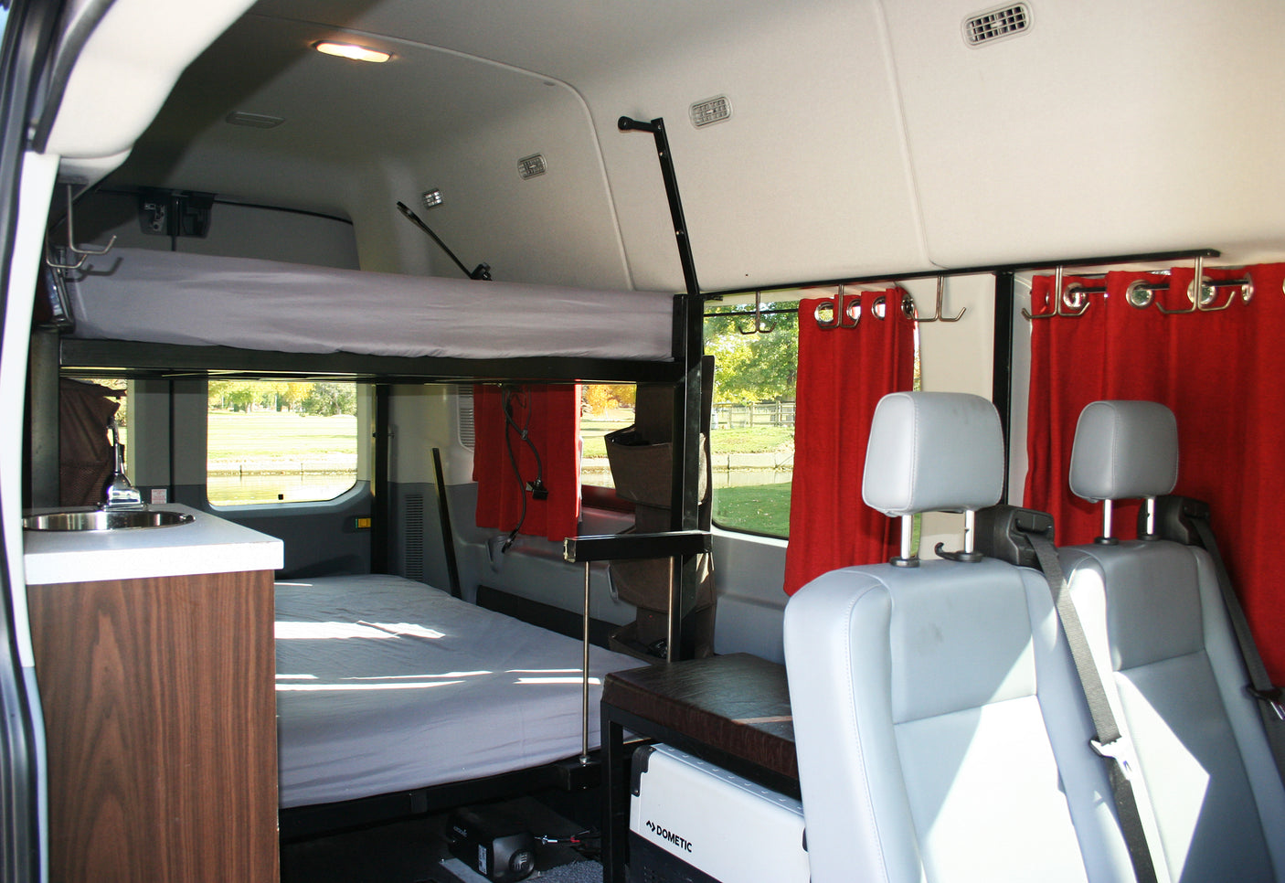 RV rental: Cozy camper interior with bunk beds, sink, seats, and red curtains, offering a home-like travel experience.
