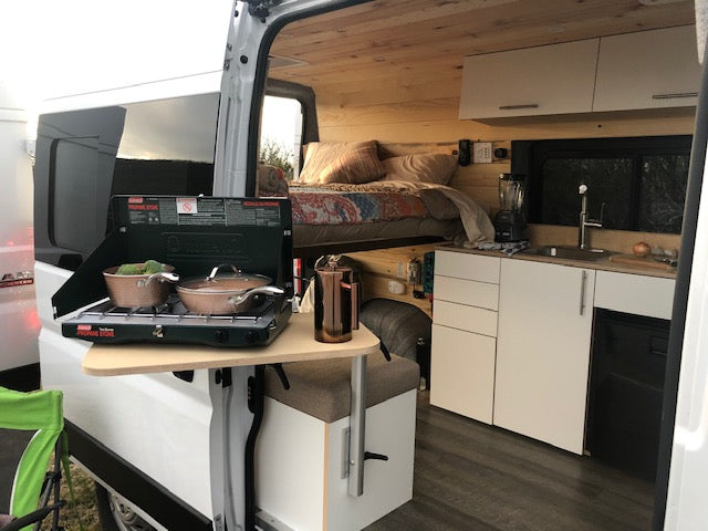 This rv rental features a cozy interior with a built-in kitchen, elevated bed, and outdoor propane stove setup for versatile camping.