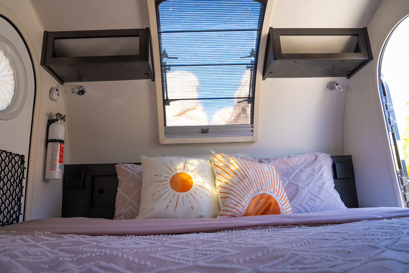 Relaxing RV rental interior: a comfy bed with decorative sun pillows, overhead skylight, and wall storage.