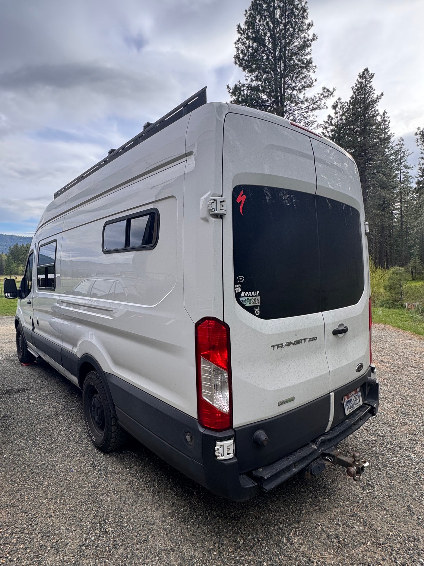 White Ford Transit camper van, ideal for your next rv rental adventure, parked on gravel surrounded by nature.