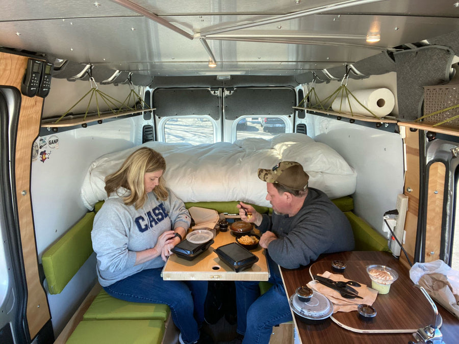 sits on a gravel lot.|Inside a comfy rv rental camper: a woman on the bed