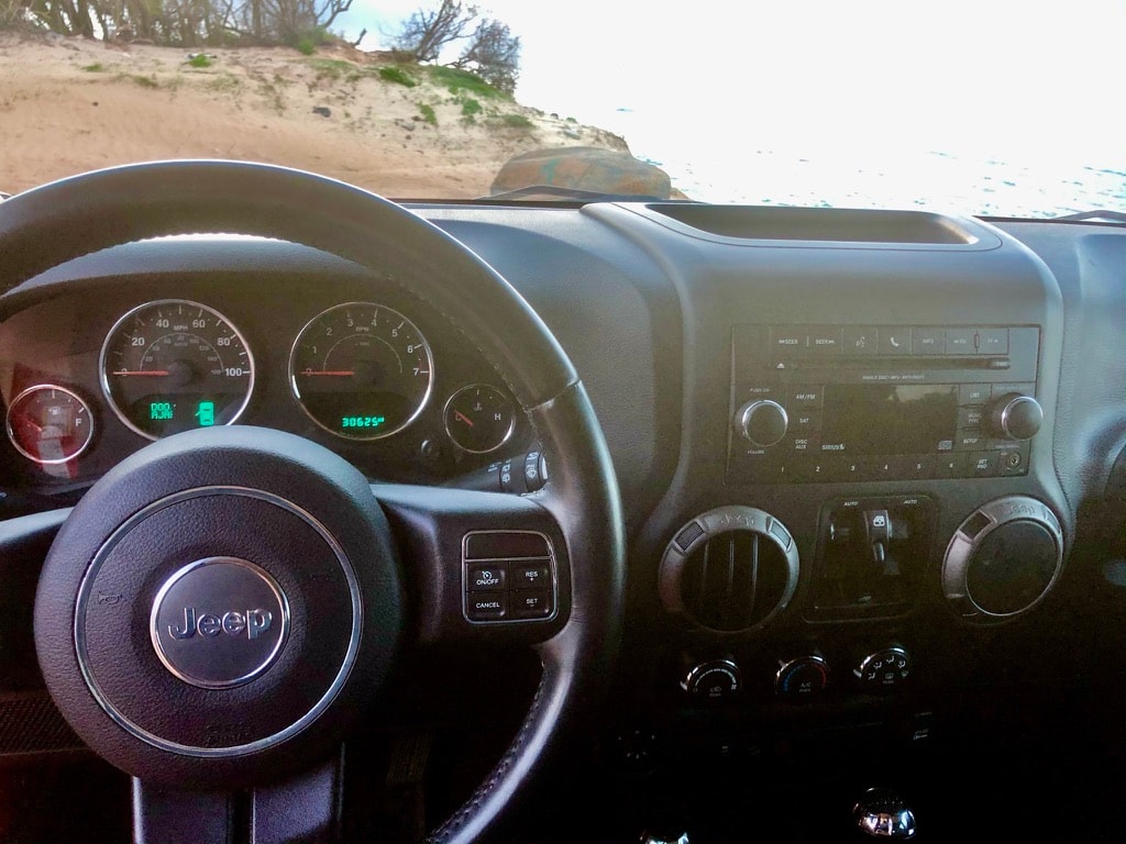Dashboard view from a Jeep Wrangler, showing steering wheel and 30625 miles, parked on sand. Consider for your RV rental journey.
