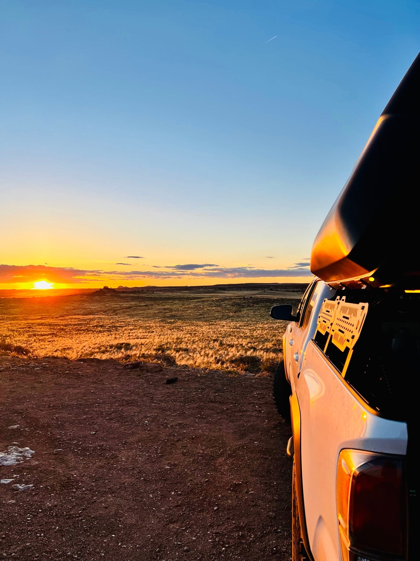 White pickup truck with rooftop camper faces a golden sunset over fields. Ideal RV rental scene for nature exploration.