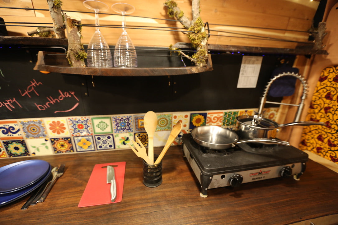 RV rental kitchen showing a portable stove, wooden utensils, blue plates, and a 'Happy 49th Birthday' chalkboard message.