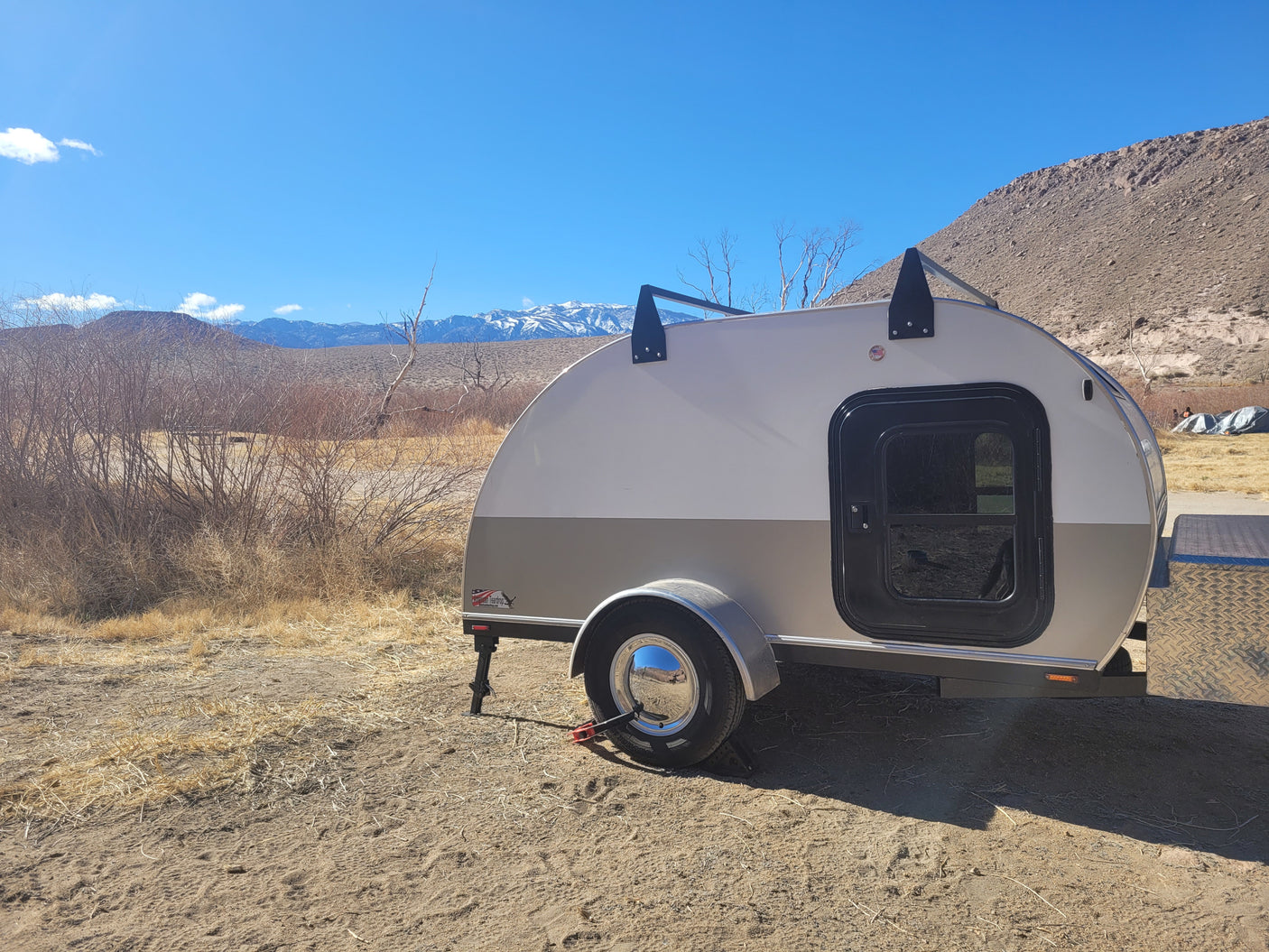 RV rental teardrop camper parked in a sunny, dry landscape with distant snow-capped mountains. Perfect for outdoor travel.