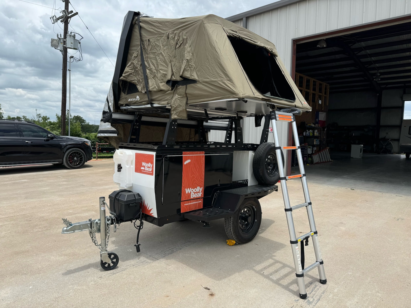 A "Woolly Bear" overland trailer with a rooftop tent and ladder, ideal for your next RV rental adventure.