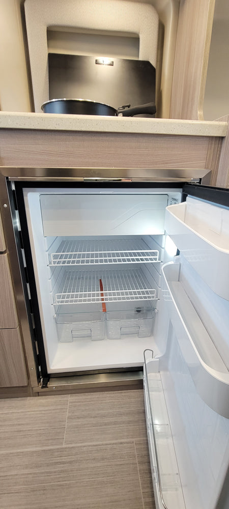 New, empty compact fridge/freezer in an rv rental kitchen, ready for your travel essentials. Shows shelves and drawers.
