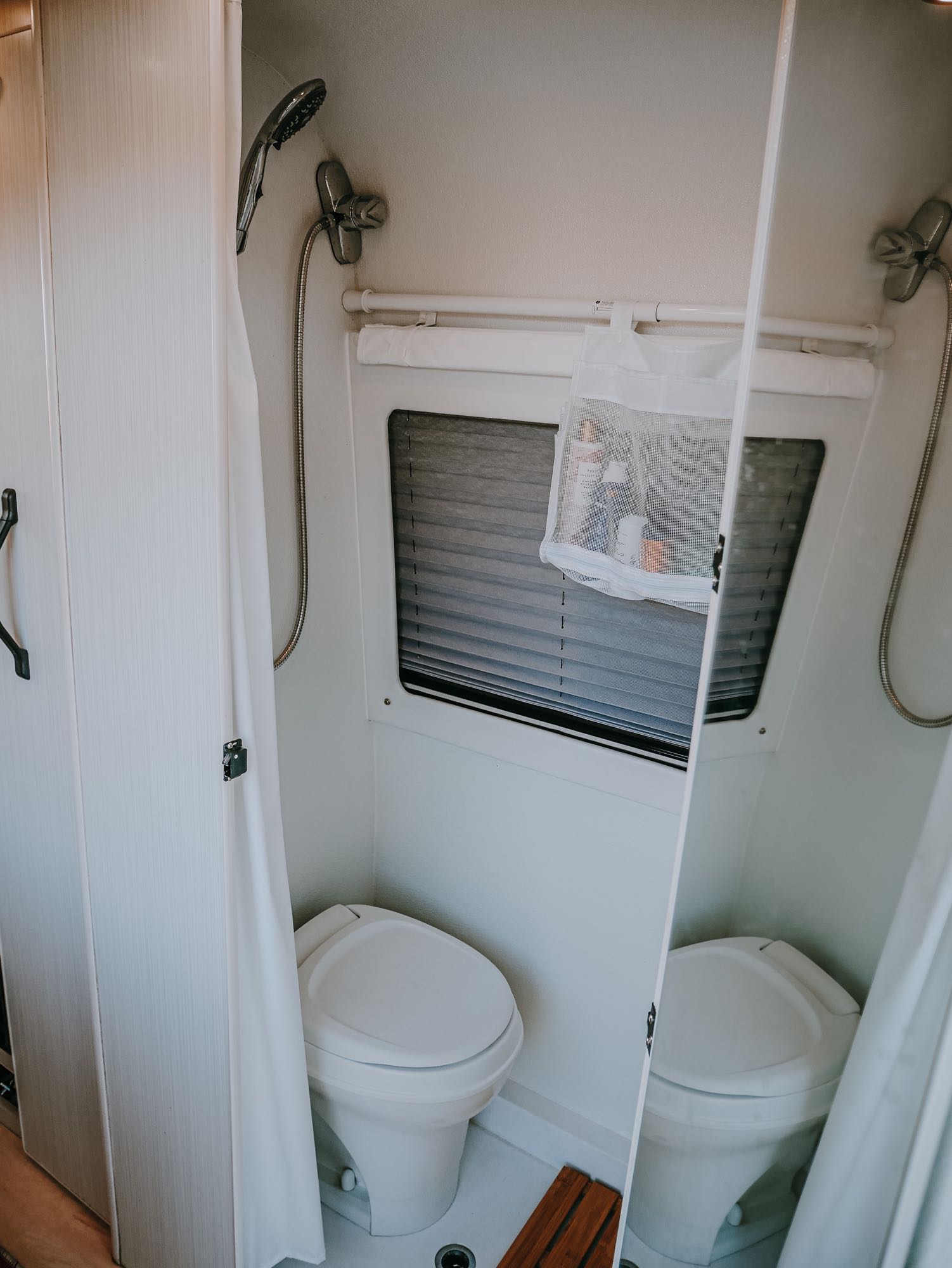 A compact, modern RV rental bathroom features a toilet, shower, and a mesh caddy with toiletries.