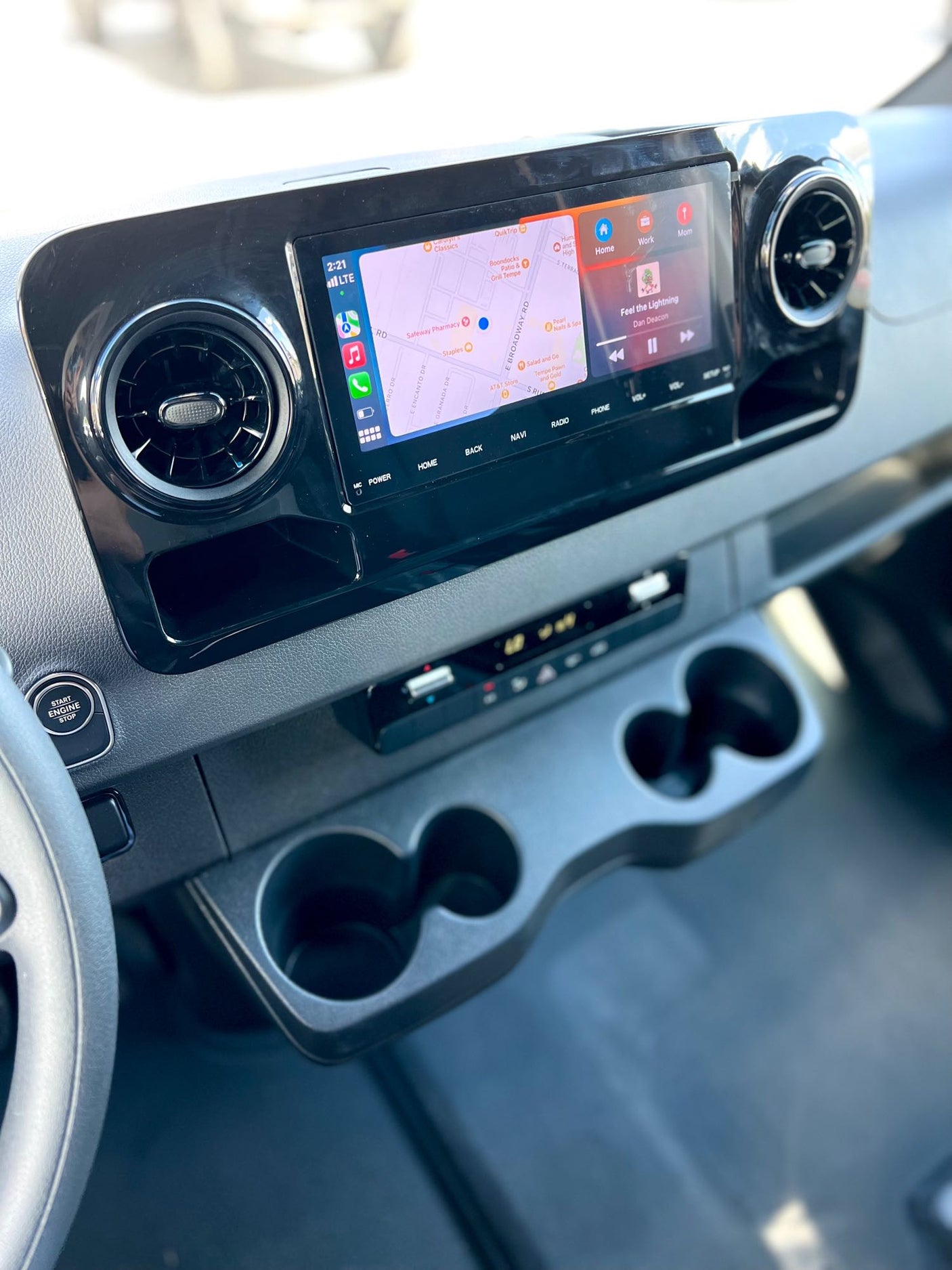 Explore this modern RV rental's dashboard: a large touchscreen shows navigation & music, with start button & cup holders visible.