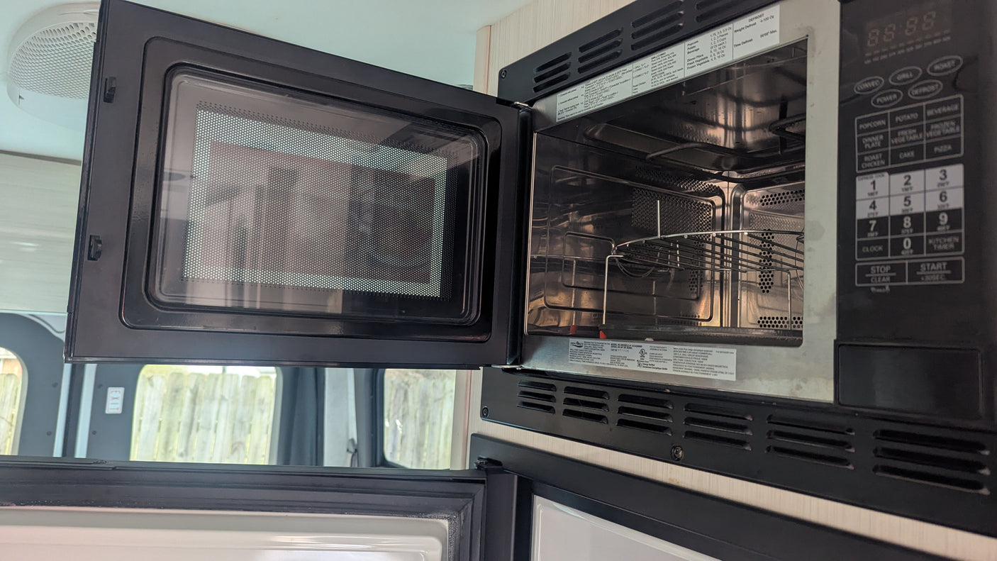 RV rental interior: Open microwave/convection oven, showing its metal rack and digital controls, ready for cooking.