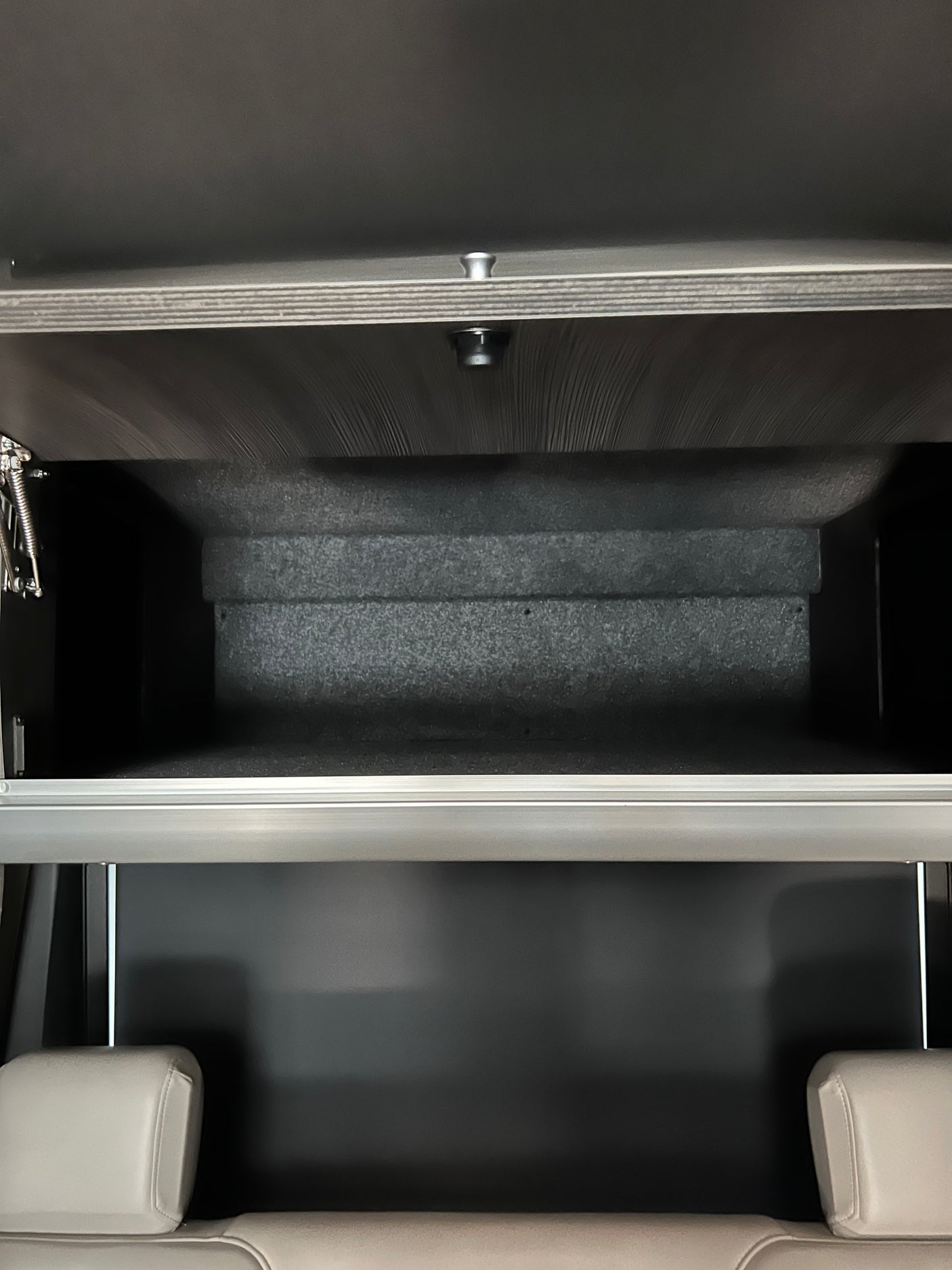 Open overhead storage in an RV rental, revealing a dark, lined interior above light-colored passenger seats.