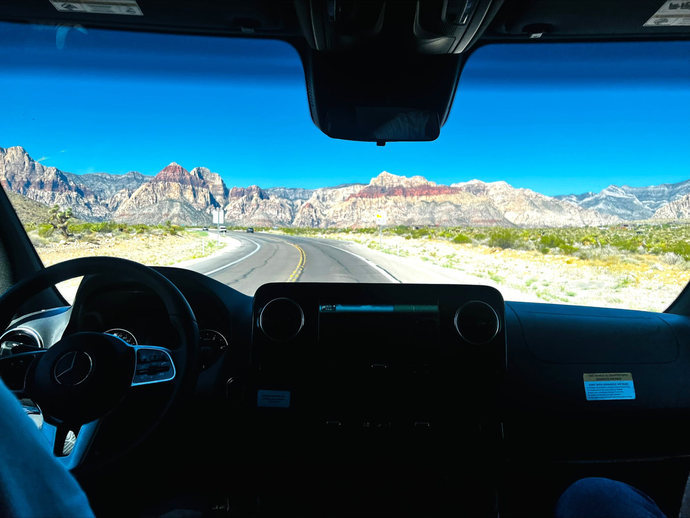 RV rental journey: A Mercedes-Benz drives through a scenic desert with colorful mountains under a bright blue sky.
