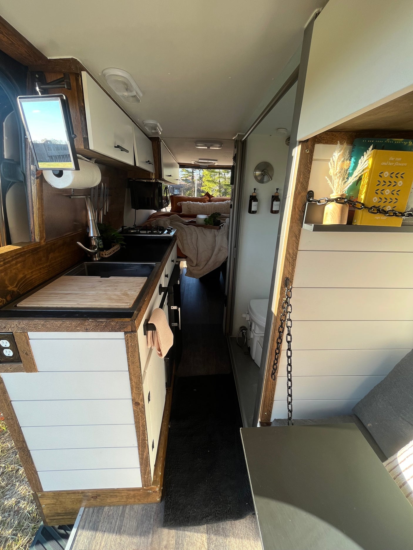 This RV rental showcases a narrow, inviting interior with a kitchen, bed area, and a side bathroom. Wood & white decor.