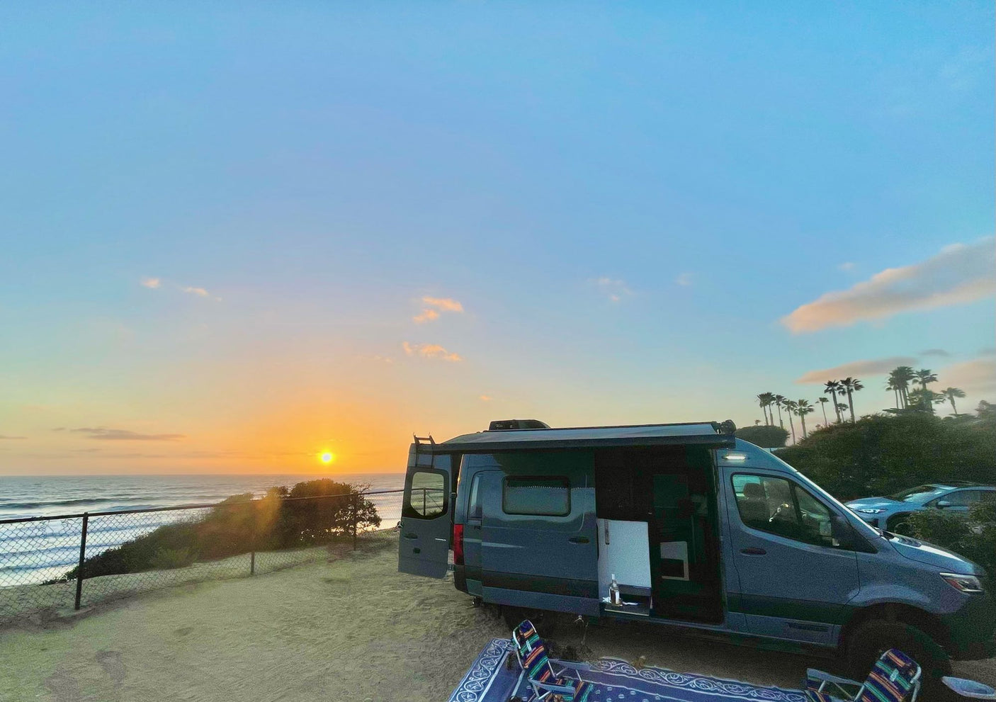 Enjoying a stunning beach sunset from an RV rental, parked seaside with doors open, showcasing ocean views and a peaceful setting.