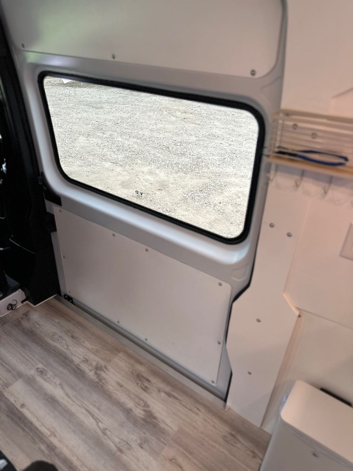 Spacious RV rental interior showing a large window looking onto gravel, light wood-look flooring, and clean white paneling.
