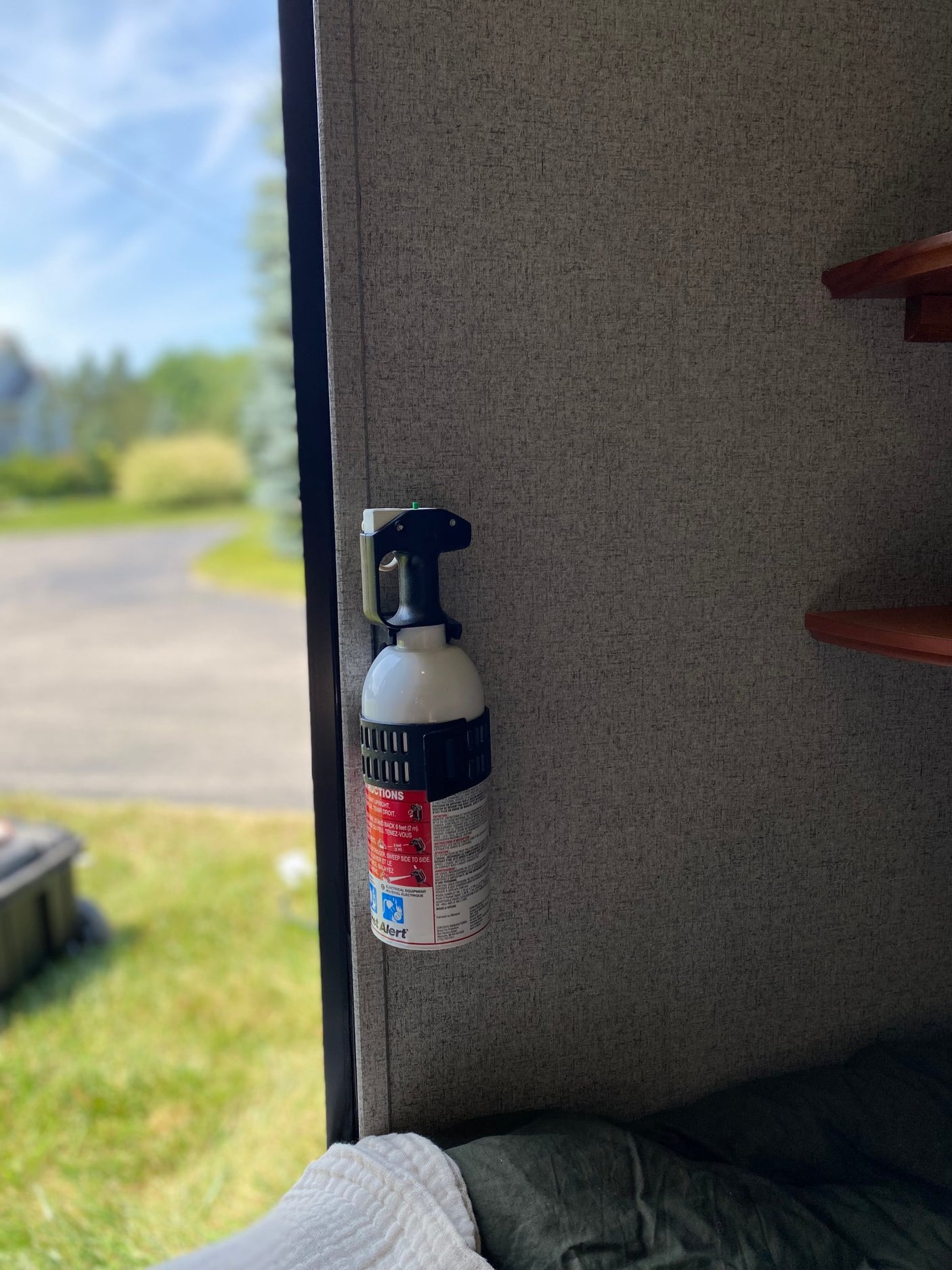 Inside an RV rental, a First Alert fire extinguisher is mounted on the wall, ensuring safety with a sunny outdoor view.