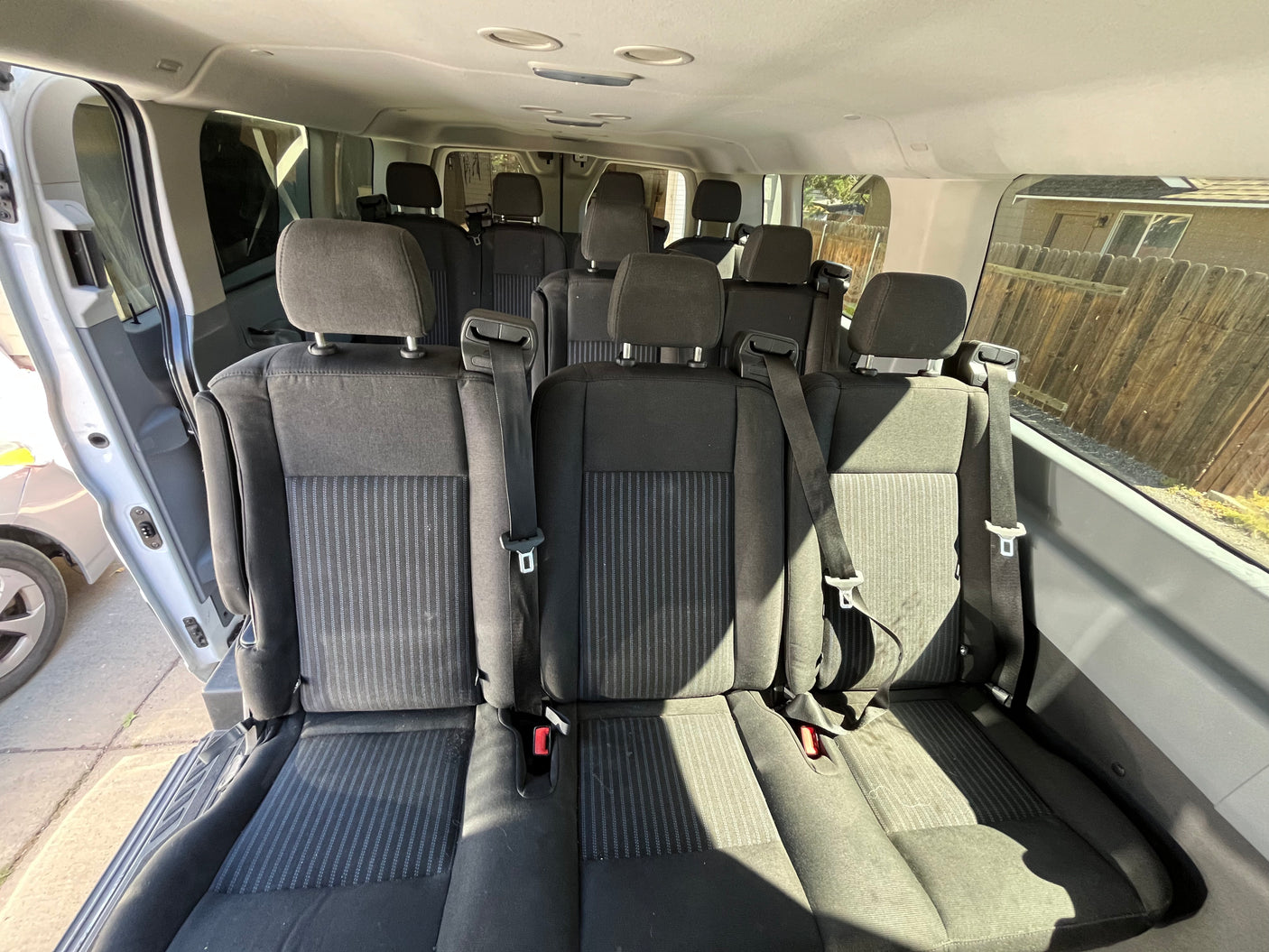 Spacious interior of an RV rental passenger van, featuring multiple rows of black fabric seats with headrests and seatbelts.