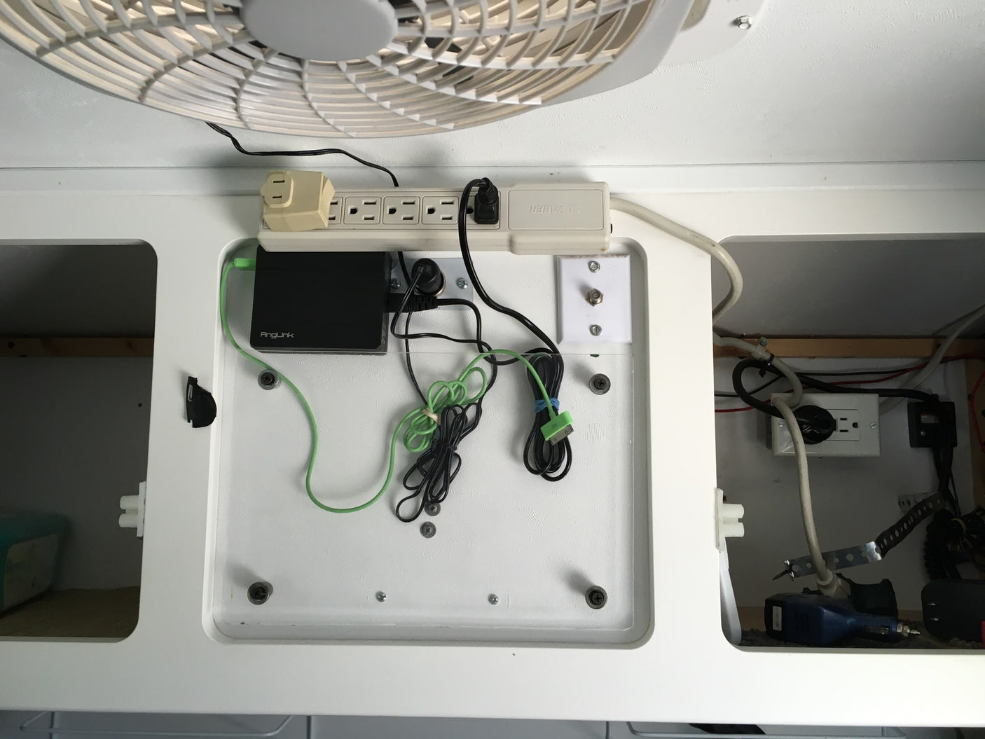 RV rental power setup: A wall-mounted station with power strip, AngLink hub, various charging cables, and electrical outlets for devices.