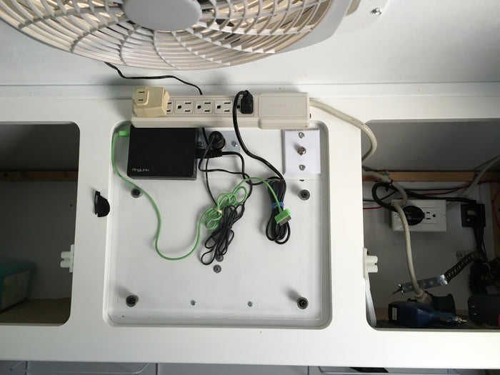 RV rental power setup: A wall-mounted station with power strip, AngLink hub, various charging cables, and electrical outlets for devices.